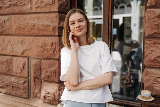 Kaukasische Frau, die im weißen T-Shirt lächelt, schaut in die Kamera