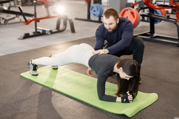 Kostenloses Foto kaukasische frau, die übungen im fitnessstudio mit einem persönlichen männlichen trainer macht