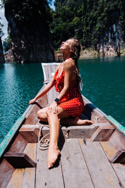 Kaukasische frau im roten sommerkleid auf thailändischem asiatischem boot im urlaub, reisen um thailand