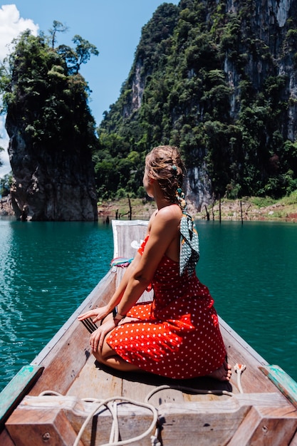 Kaukasische Frau im roten Sommerkleid auf thailändischem asiatischem Boot im Urlaub, reisen um Thailand