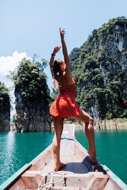 Kaukasische Frau im roten Sommerkleid auf thailändischem asiatischem Boot im Urlaub, reisen um Thailand