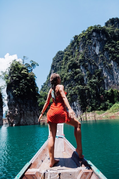 Kaukasische Frau im roten Sommerkleid auf thailändischem asiatischem Boot im Urlaub