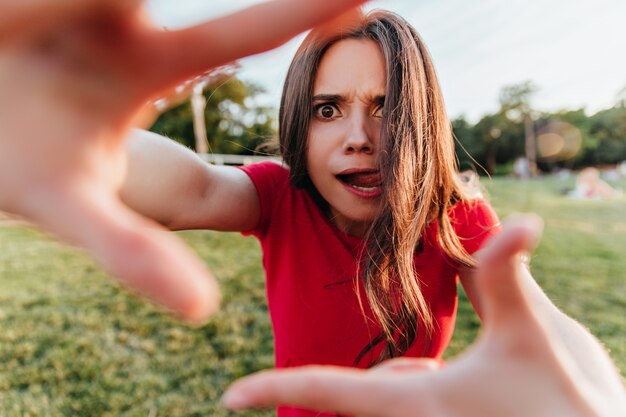 Kaukasische Frau in guter Laune, die im Park spielt. Außenaufnahme des positiven weiblichen Modells, das während des Fotoshootings unter freiem Himmel herumalbert.