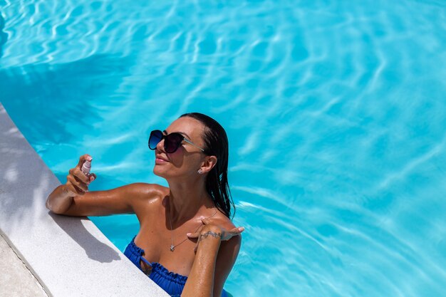 Kaukasische gebräunte Frau glänzende Bronzehaut durch Pool im blauen Bikini am sonnigen Tag