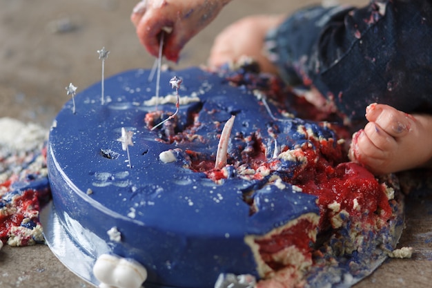 kaukasische Geburtstagsbabyarme beim Zerstören und zertrümmert blauen Glasurkuchen