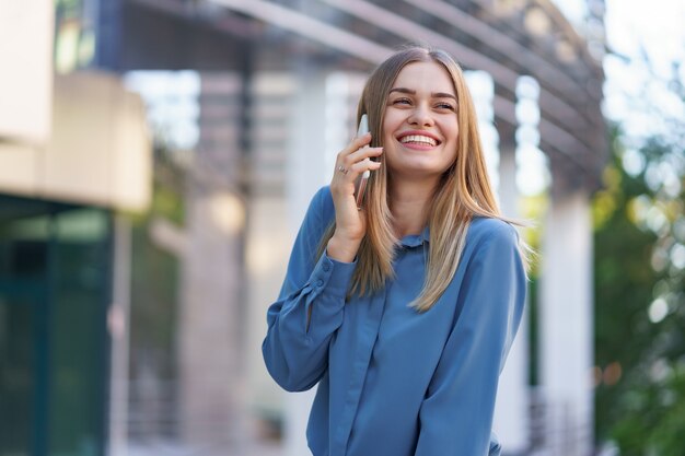 Kaukasische Geschäftsfrau, die telefonisch Kaffee hält, um zu gehen. Eine erfolgreiche europäische Frau, die am Telefon spricht und auf einem modernen Bürogebäude steht