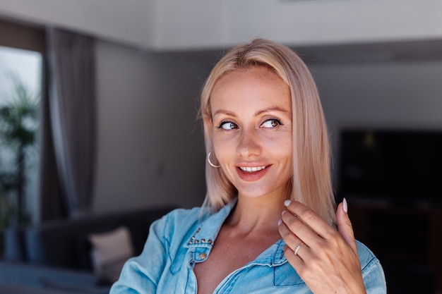 Kaukasische hübsche blonde Frau des kurzen Haares in der Jeansjacke, die Haar mit rosa Haarbürste zu Hause bürstet