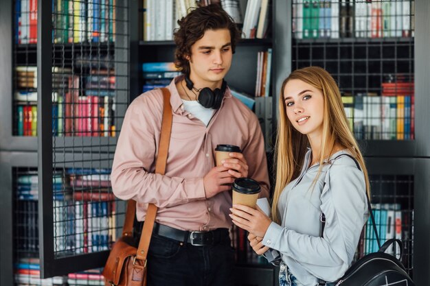 Kaukasische junge Studentin und Studentin liest Buch in der Institutsbibliothek mit einer Tasse Kaffee