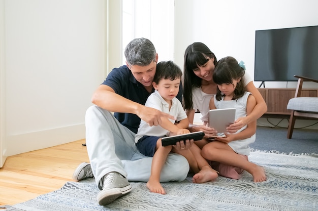 Kaukasische Mama und Papa umarmen Kinder, benutzen Tablets und Telefon und lächeln.