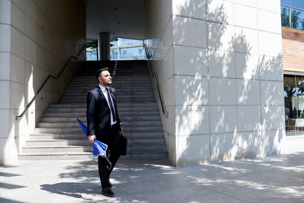 Kaukasischer Geschäftsmann in der Klage mit Regenschirm gehend vor Büro und Treppenhaus