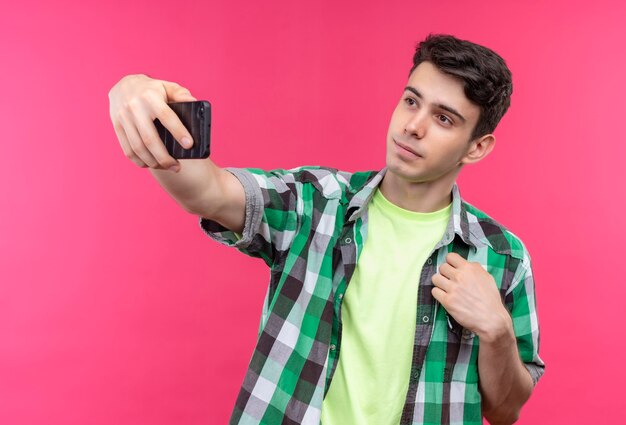 Kaukasischer junger Mann, der grünes Hemd trägt, nimmt ein Selfie auf isolierter rosa Wand