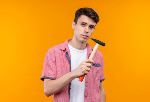 kaukasischer junger Mann, der rosa Hemd hält Hammer auf isolierter orange Wand hält