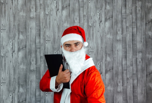 Kaukasischer junger mann verkleidet als weihnachtsmann wütend mit laptop in der hand. weihnachtsverkaufskonzept