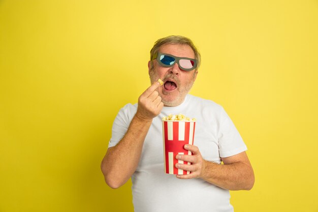 Kaukasischer Mann, der Kino mit Popcorn und 3D-Brille auf Gelb beobachtet