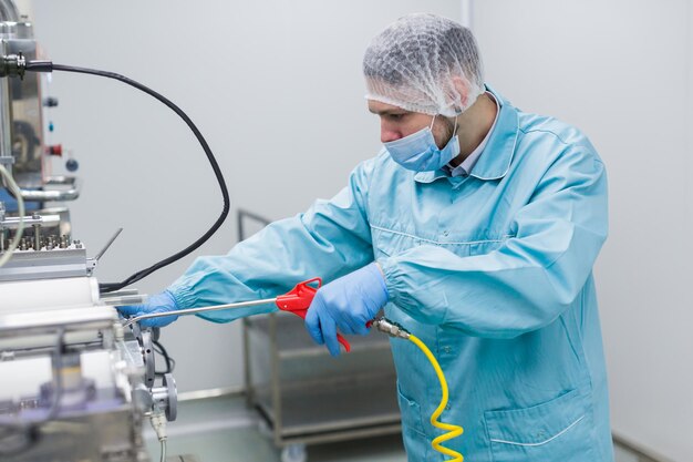 Kaukasischer Wissenschaftler in blauer Laboruniform konfiguriert Fertigungsmaschine mit Wellen und Bedienfeld Bild schließen