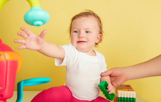 Kaukasisches kleines Mädchen, Kinder lokalisiert auf gelbem Studiohintergrund. Porträt des niedlichen und entzückenden Kindes, des Babys, das spielt und lacht.