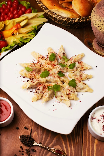 Kaukasisches traditionelles foodl dushbere, Gurze diente mit Joghurt und Tomatensauce. in weißen Teller mit Turshu auf Holztisch dekoriert