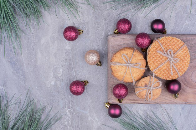 Kekse auf einem Holzbrett mit roten Glitzer-Weihnachtskugeln herum