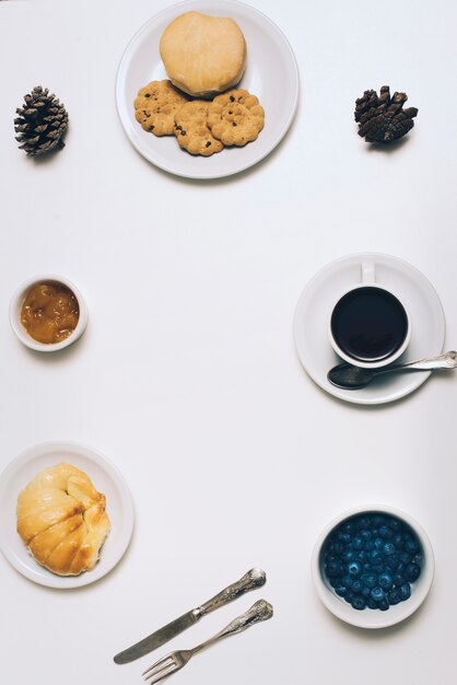 Kekse; Brot; Brötchen; Marmelade; Tannenzapfen; Blaubeeren und Kaffeetasse auf weißem Hintergrund