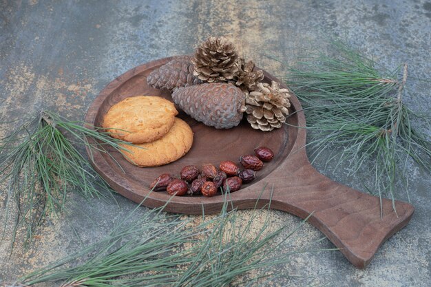 Kekse, getrocknete Hagebutten und Tannenzapfen auf Holzbrett. Hochwertiges Foto
