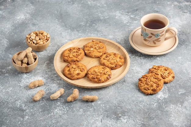 Kekse mit Bio-Erdnüssen und Honig auf Holzbrett mit Tasse Tee.