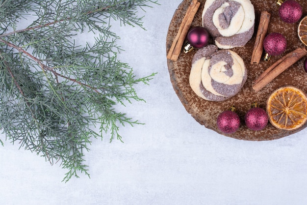 Kekse mit Kugeln, Zimt und Orangenscheiben auf Holzstück.