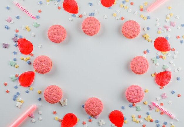 Kekse mit Zuckerstreuseln, Kerzen, Blütenblättern auf weißem Tisch