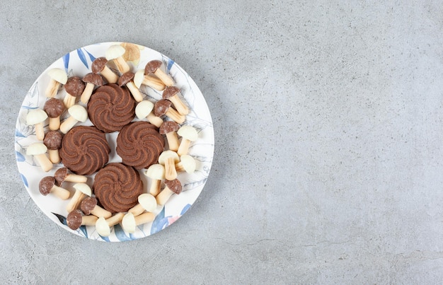 Kekse, umgeben von Schokoladenpilzen auf einem Teller auf Marmorhintergrund.