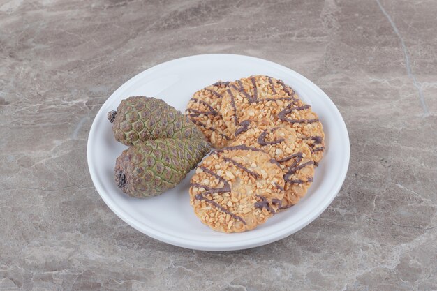 Kekse und Tannenzapfen auf einer Platte auf Marmor