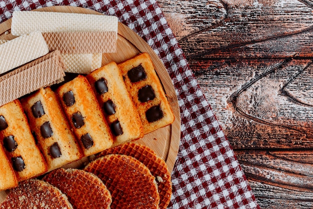 Kostenloses Foto kekse und waffeln auf einer schneidebrett-draufsicht auf einem stoff- und holzhintergrund