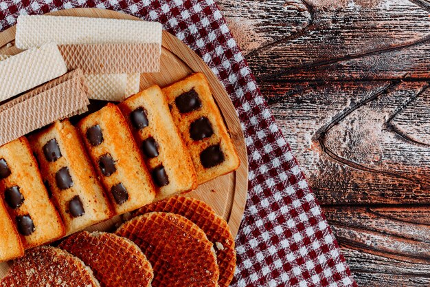 Kekse und Waffeln auf einer Schneidebrett-Draufsicht auf einem Stoff- und Holzhintergrund