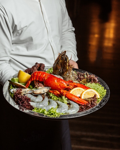 Kellner hält Meeresfrüchteplatte mit Hummer Riesengarnelen und Muscheln