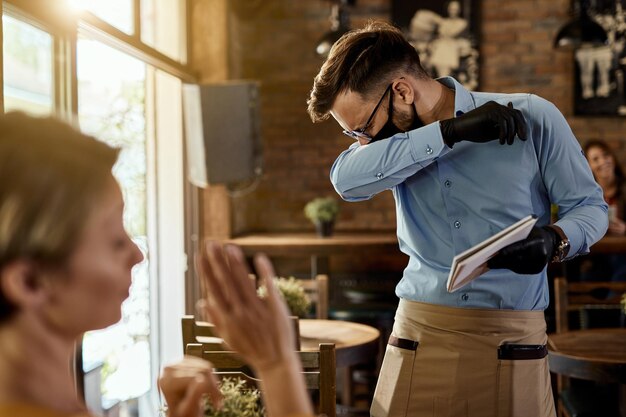 Kellner niest in den Ellbogen, während er einen Kunden in einem Café bedient