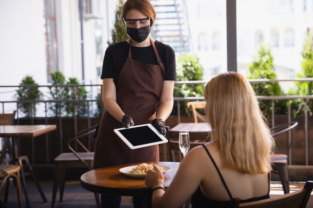 Kellnerin arbeitet in einem Restaurant in einer medizinischen Maske, Handschuhe während der Coronavirus-Pandemie