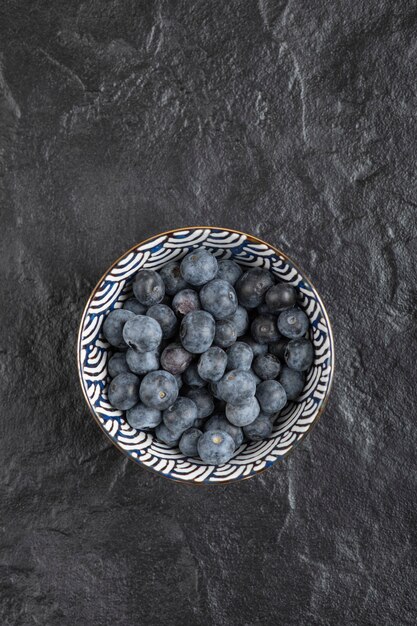 Keramikschale mit leckeren frischen Blaubeeren auf schwarzer Oberfläche