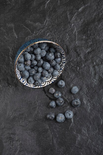 Keramikschale mit leckeren frischen Blaubeeren auf schwarzer Oberfläche