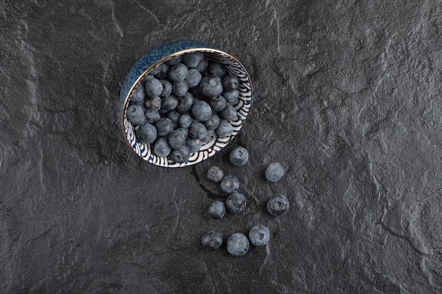 Keramikschale mit leckeren frischen Blaubeeren auf schwarzer Oberfläche