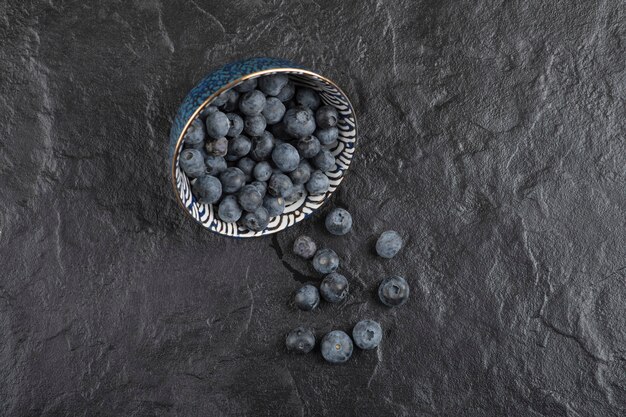 Keramikschale mit leckeren frischen Blaubeeren auf schwarzer Oberfläche