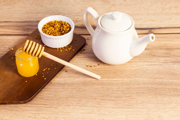 Keramische Teekanne mit dem Blütenstaub und hölzernem Hintergrund des Honigs