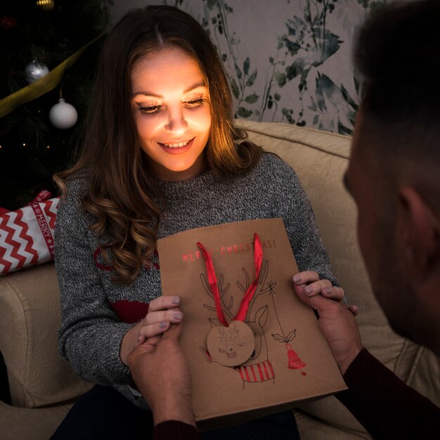 Kerl, der attraktiver Dame auf Sofa nahe Weihnachtsbaum Geschenkpaket darstellt