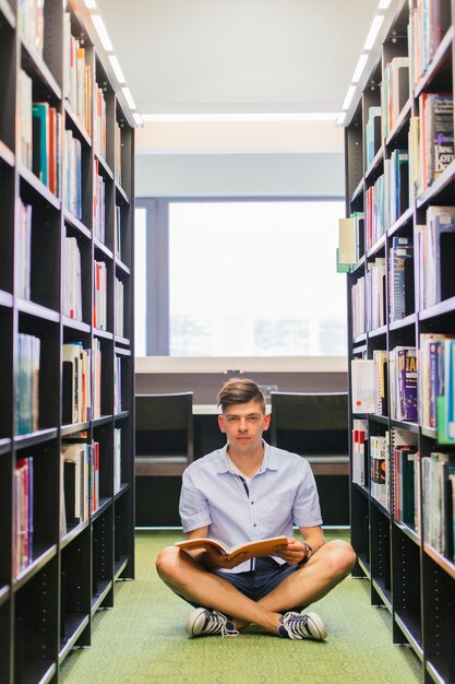 Kerl, der auf Fußboden in der Bibliothek sitzt