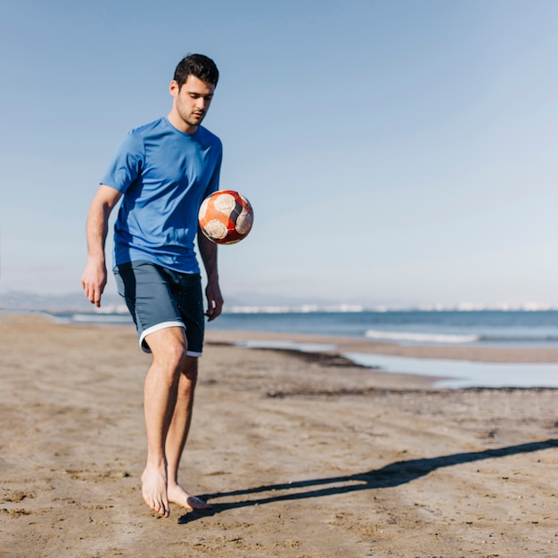 Kerl, der Fußball am Strand spielt