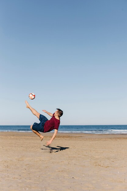 Kerl, der Fußball am Strand spielt