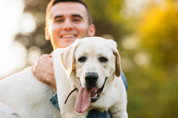 Kerl, der seinen Freundhund Labrador hält und bei Sonnenuntergang lächelt