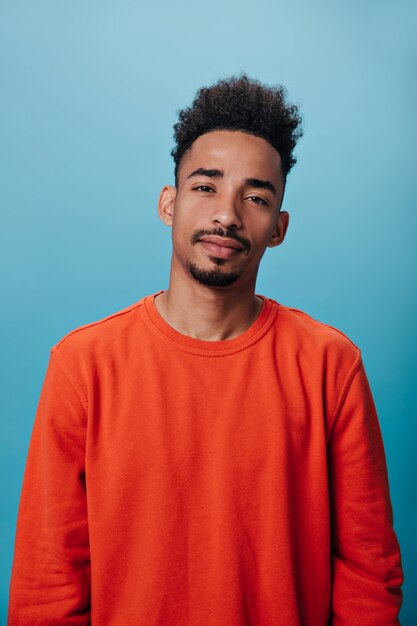 Kerl im orangefarbenen Sweatshirt schaut in die Kamera auf blauer Wand