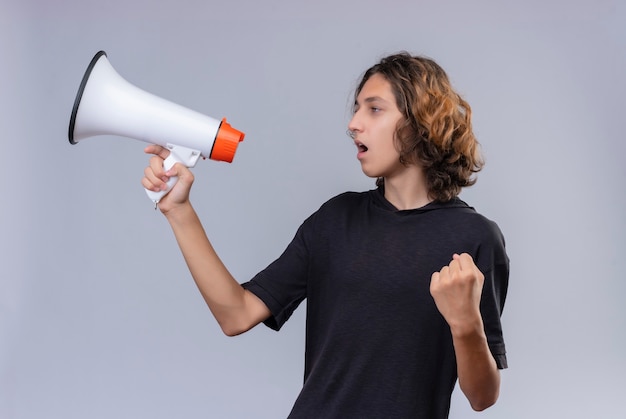 Kerl mit langen Haaren im schwarzen T-Shirt spricht durch Lautsprecher an weißer Wand