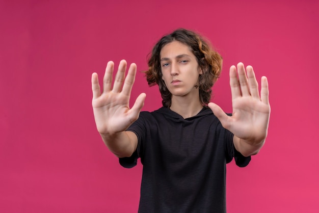 Kerl mit langen Haaren im schwarzen T-Shirt zeigt fünf mit beiden Händen an der rosa Wand