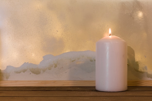 Kerze auf hölzernem Brett nahe Haufen des Schnees durch Fenster