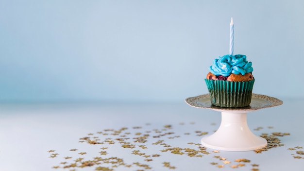 Kostenloses Foto kerze auf kleinem kuchen über dem cakestand gegen blauen hintergrund