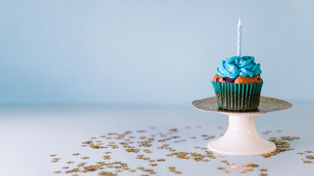 Kerze auf kleinem Kuchen über dem cakestand gegen blauen Hintergrund